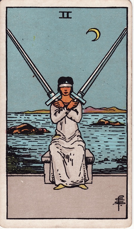 Two of swords. In this card, there is a person who is blindfolded and holding a sword in each hand. Their arms are crossed and the swords point outward in each direction.